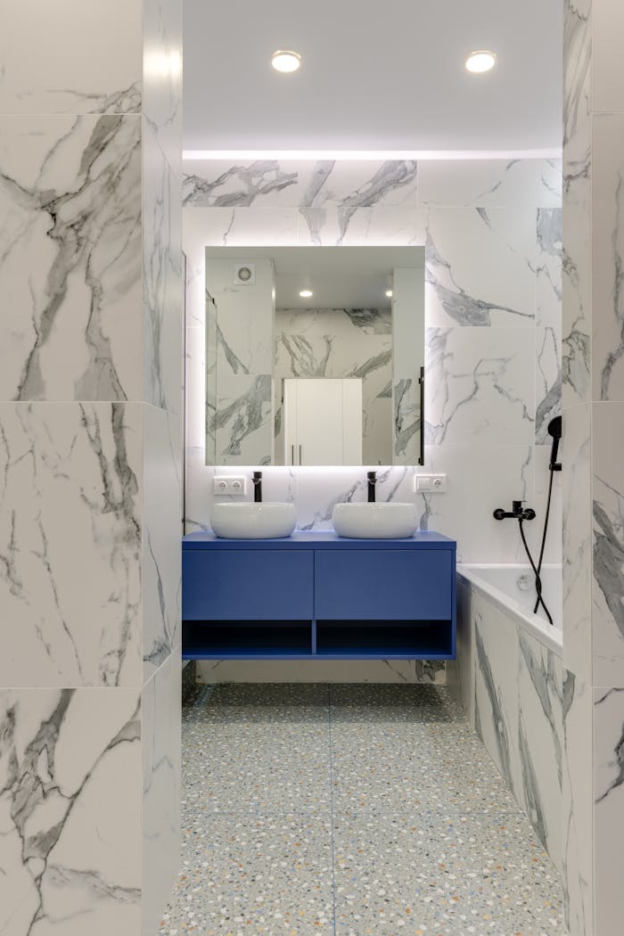 about-us Stylish marble bathroom with blue vanity and double sinks.